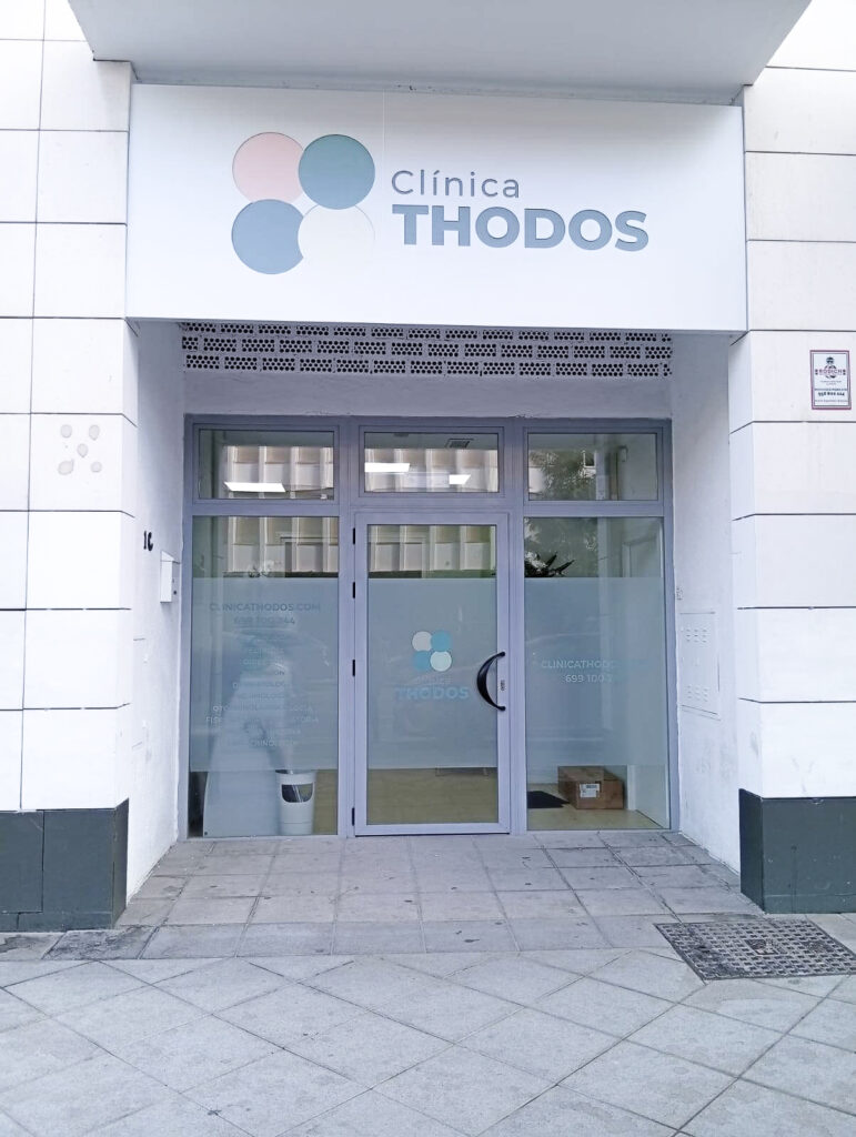 Entrada frontal de la Clínica Thodos Granada con el letrero del centro y logotipo sobre las puertas de cristal, mostrando la fachada principal de la clínica